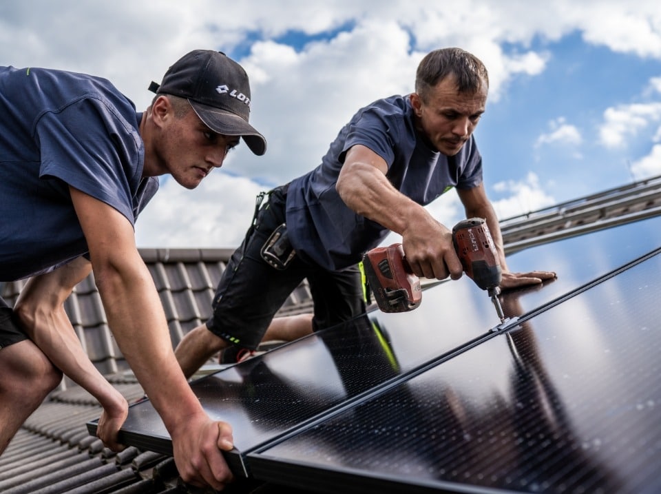 FEBESOL-Monteure bringen ein Solarpanel mit einem Akkuschrauber auf dem Dach an