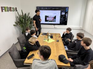 In einem Thermondo-Klassenzimmer steht ein Mann und hält auf einer großen Leinwand einer Gruppe junger Studenten an einem Konferenztisch einen Vortrag.
