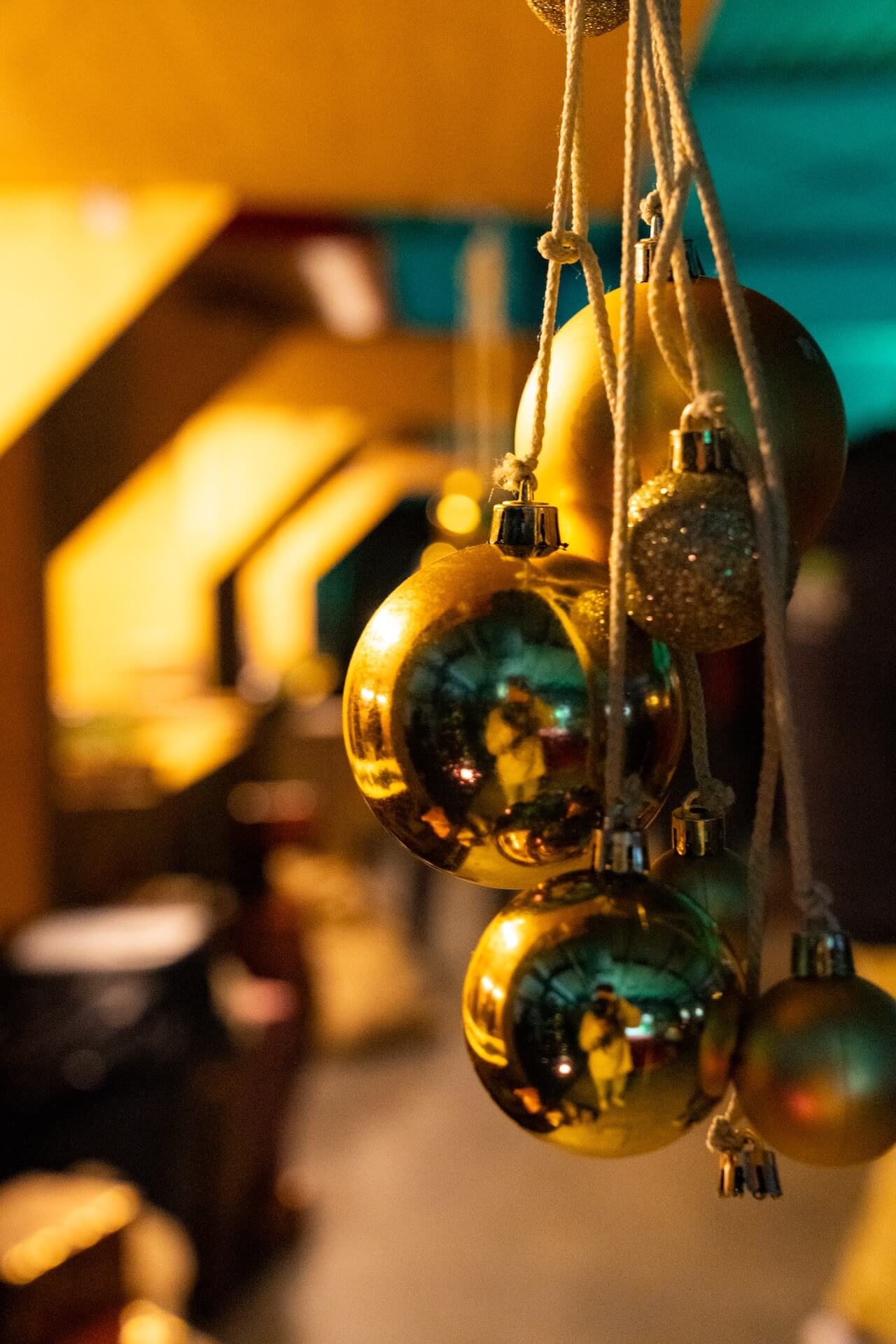 Nahaufnahme von in einer Reihe hängenden goldenen Weihnachtsdekorationen, die ein gemütliches, warm beleuchtetes Interieur widerspiegeln.