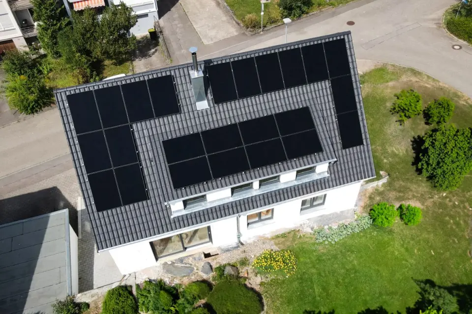 Luftaufnahme eines weißen Hauses mit Sonnenkollektoren auf dem Dach, umgeben von grünen Bäumen und einer Auffahrt.