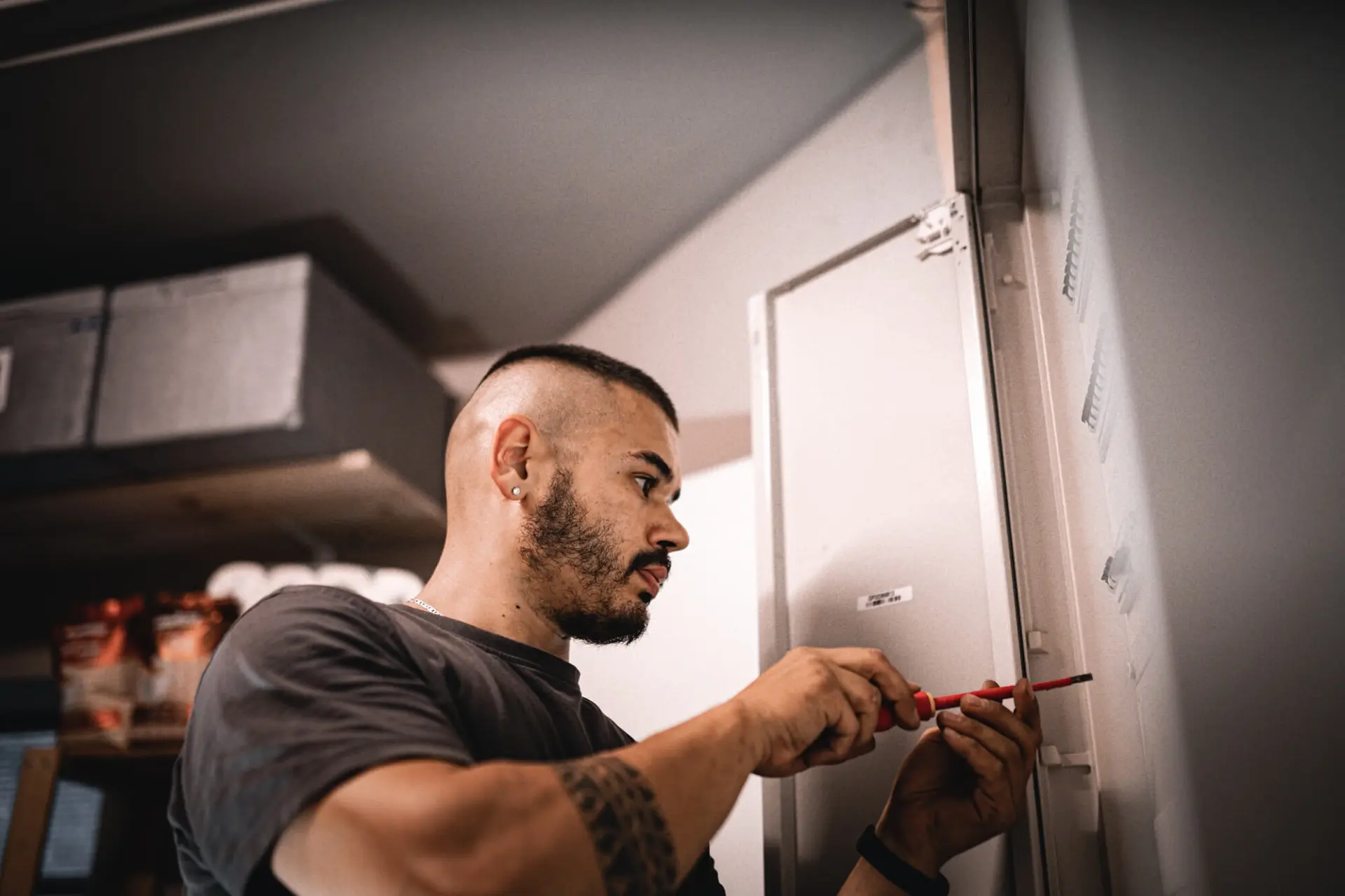 Ein bärtiger Mann arbeitet mit einem Schraubenzieher an einer Schalttafel in einem Raum und führt Wartungsarbeiten an einem Smart Grid-System durch.