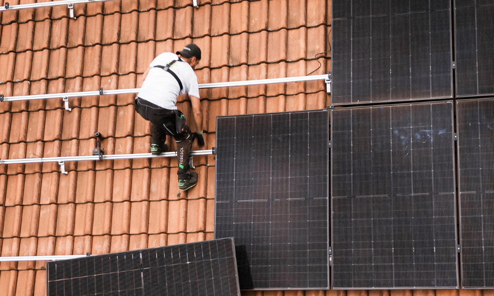 Arbeiter in einem Geschirr, das Solarpaneele auf einem Ziegeldach installiert, ein wichtiger Schritt zur effizienten Energienutzung – ähnlich wie beim Stromzähler: Was Sie über diese wichtige Technologie wissen sollten.