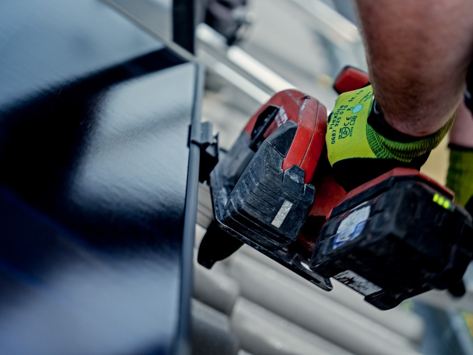 Nahaufnahme einer Person mit Handschuhen, die mit einem Elektrowerkzeug an einer Metalloberfläche arbeitet, ähnlich wie Profis Geräte installieren würden, wenn sie überlegen: „Was kostet eine PV-Anlage pro kWp?“.