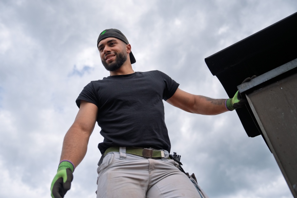 Ein Mann mit Arbeitshandschuhen und Mütze steht lächelnd auf einem Dach, im Hintergrund ein bewölkter Himmel – bereit zur Installation von „Photovoltaik ohne Speicher“.