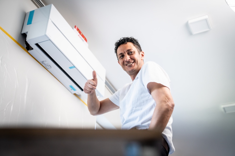 Ein Mann zeigt den Daumen nach oben, während er in der Nähe einer an der Wand montierten Klimaanlage steht.