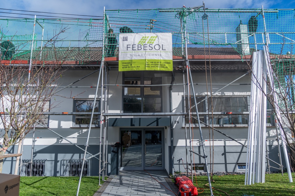 Ein Haus, das gerade renoviert wird, mit Gerüsten, Netzen und einem "FEBESOL Solartechnik"-Banner über dem Eingang.